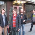 Four members of Chapterhouse standing on a city sidewalk beside their road cases and gear, left to right Stephen Patman, Greg Moore, Ashley Bates, and Andy Sherriff