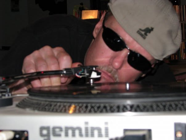 Bill Fitzhugh in a flat cap and sunglasses leaning in close to a Gemini turntable