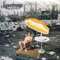 Album cover for Supertramp's Crisis? What Crisis?, showing a man relaxing under a beach umbrella in a bleak industrial landscape.
